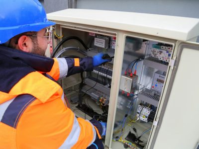 Engineer in safety gear working on an outdoor electrical panel, ensuring system functionality.